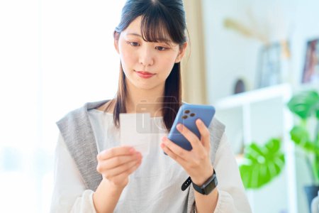 Téléchargez les photos : Jeune femme tenant un reçu et smartphone dans la chambre - en image libre de droit