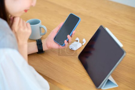 Téléchargez les photos : Une main de femme regardant l'écran d'un smartphone et d'une tablette PC sur la table - en image libre de droit
