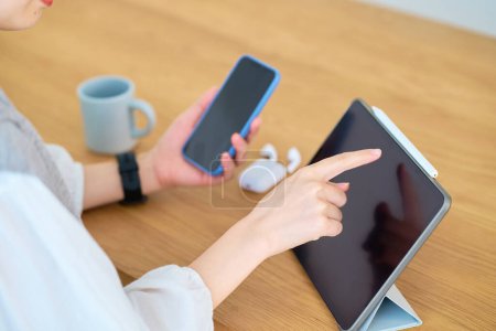 Téléchargez les photos : Une main de femme regardant l'écran d'un smartphone et d'une tablette PC sur la table - en image libre de droit