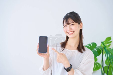 Téléchargez les photos : Jeune femme pointant vers smartphone à l'intérieur - en image libre de droit
