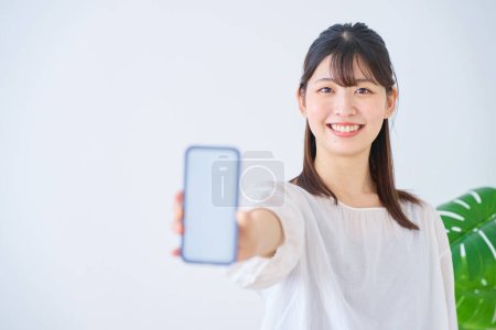 Photo for Young woman showing smartphone screen indoors - Royalty Free Image