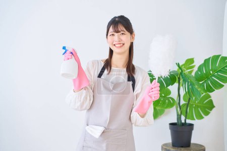 Téléchargez les photos : Jeune femme dans un tablier tenant des outils de nettoyage à l'intérieur - en image libre de droit