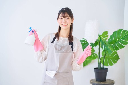 Foto de Mujer joven en un delantal sosteniendo herramientas de limpieza en el interior - Imagen libre de derechos