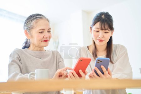 Photo for Senior woman and young woman operating smartphones in the room - Royalty Free Image