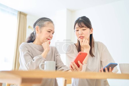 Foto de Una mujer mayor y una mujer joven mirando ansiosamente las pantallas de sus teléfonos inteligentes en el interior - Imagen libre de derechos