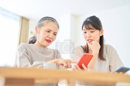 Photo for A senior woman and a young woman looking anxiously at their smartphone screens indoors - Royalty Free Image