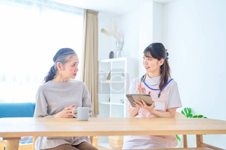 Photo for Young woman in apron and senior woman having a conversation at home - Royalty Free Image
