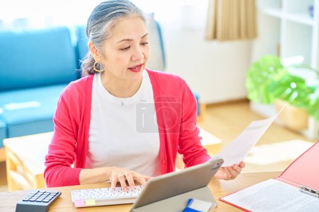 Téléchargez les photos : Une femme âgée qui fait fonctionner un ordinateur dans une pièce lumineuse - en image libre de droit