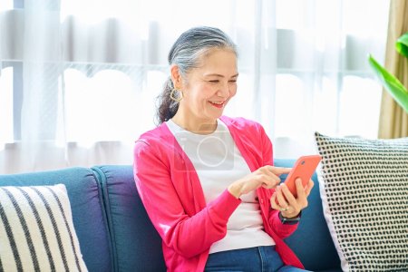 Téléchargez les photos : Femme âgée opérant un smartphone dans la chambre - en image libre de droit