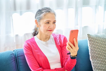 Photo for Senior woman looking at smartphone screen indoors - Royalty Free Image