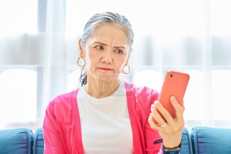 Téléchargez les photos : Une femme âgée regardant son écran de smartphone avec une expression troublée à l'intérieur - en image libre de droit