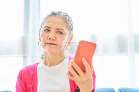 A senior woman looking at her smartphone screen with a troubled expression indoors