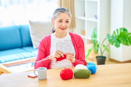 Photo for Senior woman enjoying knitting yarn in the room - Royalty Free Image