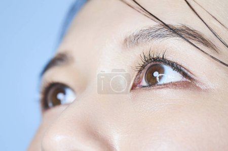 Téléchargez les photos : Gros plan des yeux d'une femme et fond bleu pâle - en image libre de droit