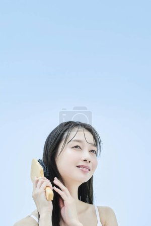 Téléchargez les photos : Femme aux cheveux longs brossant ses cheveux avec le sourire - en image libre de droit