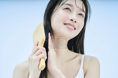 Photo for Long-haired woman brushing her hair with smile - Royalty Free Image