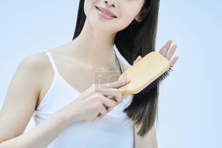 Téléchargez les photos : Femme aux cheveux longs brossant ses cheveux avec le sourire - en image libre de droit