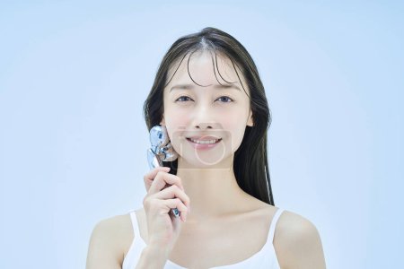 Young woman self-massaging her face and pale blue background
