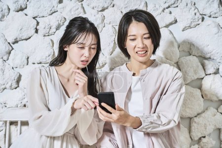 Foto de Dos mujeres mirando las pantallas de sus teléfonos inteligentes con expresiones sospechosas - Imagen libre de derechos