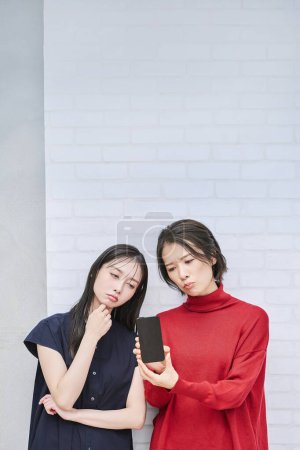 Foto de Dos mujeres mirando sus teléfonos inteligentes con expresiones ansiosas - Imagen libre de derechos