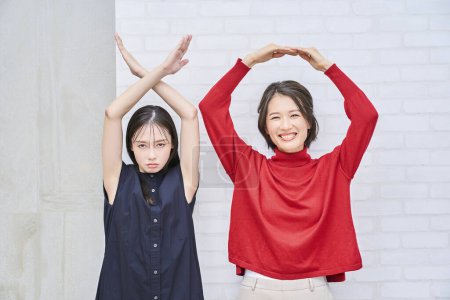 Téléchargez les photos : Deux femmes faisant cercle et croix signes de la main à l'intérieur - en image libre de droit