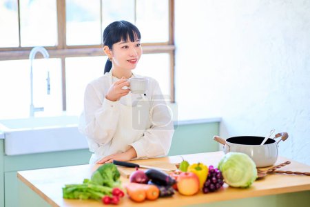 Téléchargez les photos : Jeune femme relaxante dans la cuisine et légumes alignés sur la table - en image libre de droit