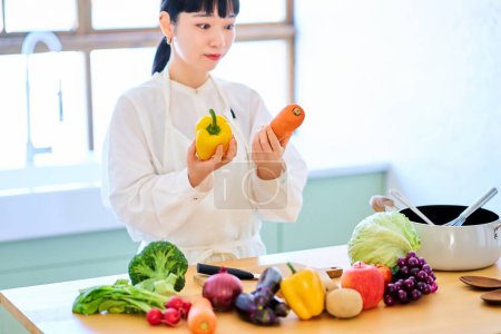 Téléchargez les photos : Jeune femme ramasser des légumes dans la cuisine - en image libre de droit