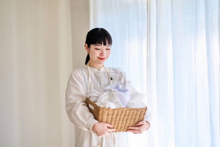 Photo for Young woman standing by the window with laundry - Royalty Free Image