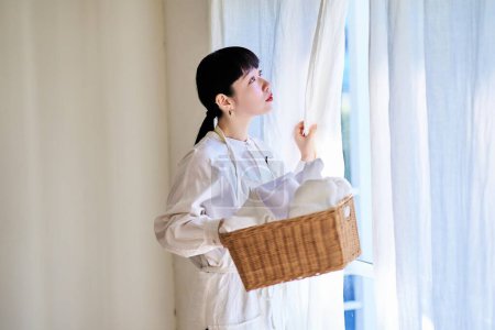 Photo for Young woman standing by the window with laundry - Royalty Free Image