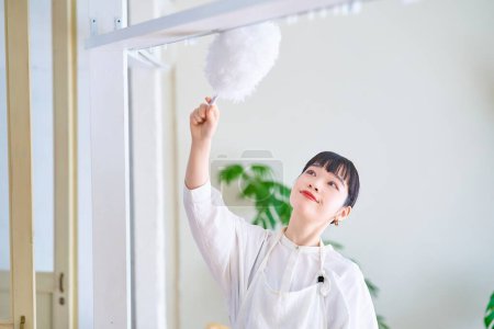 Téléchargez les photos : Jeune femme nettoyant la poussière de tous les coins de la pièce - en image libre de droit