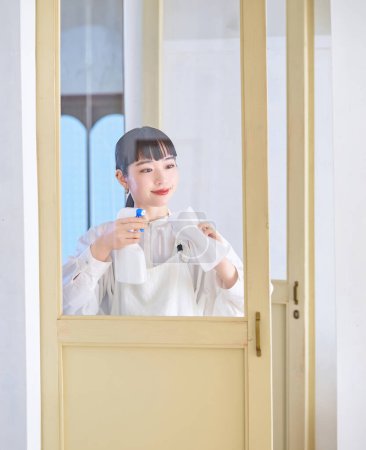 Téléchargez les photos : Jeune femme nettoyer le verre dans la chambre - en image libre de droit