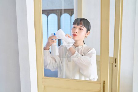 Mujer joven limpiando el vidrio en la habitación