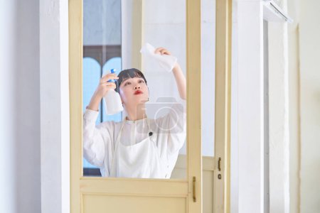Téléchargez les photos : Jeune femme nettoyer le verre dans la chambre - en image libre de droit