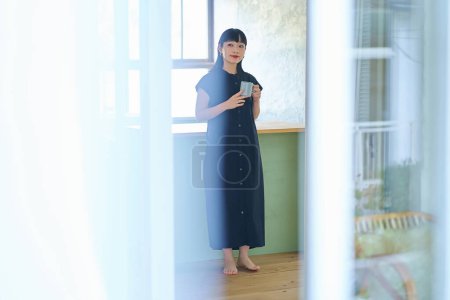 Téléchargez les photos : Jeune femme se détendre dans sa chambre avec une tasse - en image libre de droit