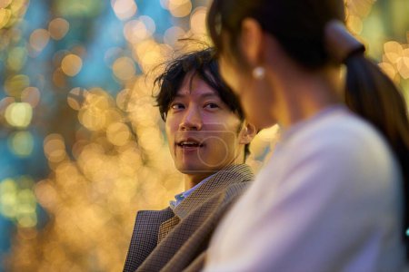 Téléchargez les photos : Un homme parlant joyeusement à une femme dans un paysage urbain éclairé - en image libre de droit