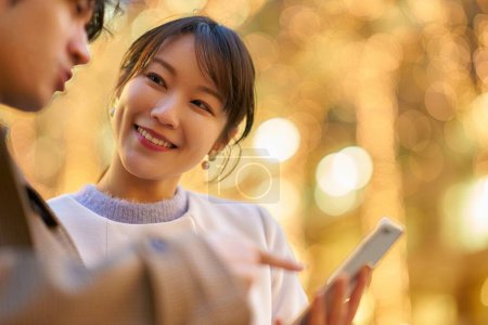 Téléchargez les photos : Une femme et un homme actionnent joyeusement leur smartphone dans une ville éclairée - en image libre de droit