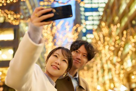 Téléchargez les photos : Un homme et une femme aiment prendre des photos lors d'une vue nocturne des illuminations - en image libre de droit