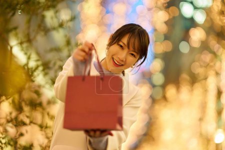 Foto de Una mujer sosteniendo una bolsa de papel y el paisaje urbano brillando con iluminaciones - Imagen libre de derechos
