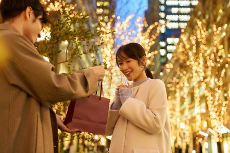 Photo for Man and woman holding gifts and a cityscape illuminated at night - Royalty Free Image