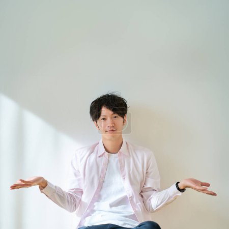 A young man poses as if comparing two options in front of a white background           