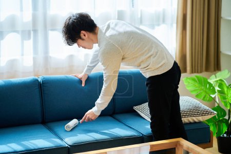Téléchargez les photos : Jeune homme nettoyer le canapé dans la chambre - en image libre de droit