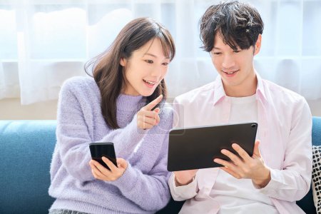 Téléchargez les photos : Un homme et une femme comparant smartphone et tablette écran PC dans la chambre - en image libre de droit