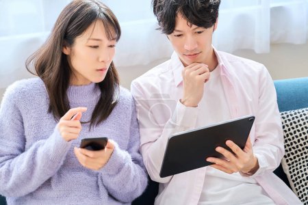 Foto de Un hombre y una mujer que comparan la pantalla del teléfono inteligente y la tableta en la habitación - Imagen libre de derechos