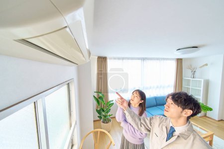 A man in work clothes standing in front of an air conditioner and a woman watching over it