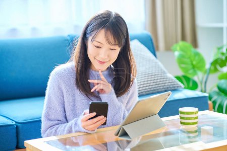 Téléchargez les photos : Une femme comparant les écrans de son smartphone et de sa tablette PC - en image libre de droit