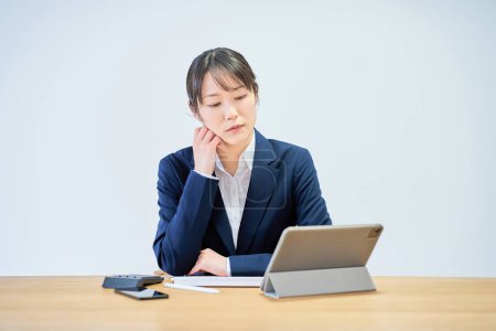 A woman in a suit working at a desk looking tired