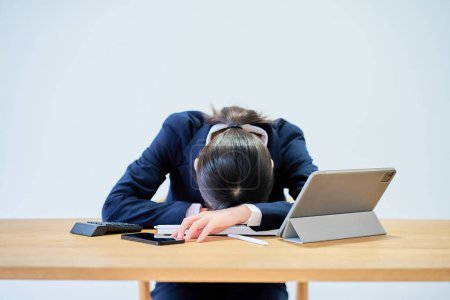 Eine Frau im Anzug, die am Schreibtisch arbeitet, sieht müde aus