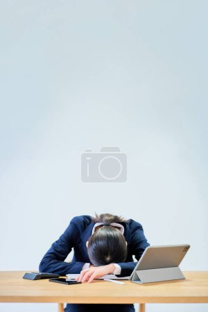 Photo for A woman in a suit working at a desk looking tired - Royalty Free Image