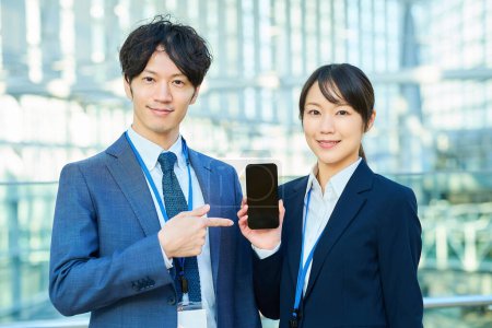 Young man and woman in suits showing smartphone screens