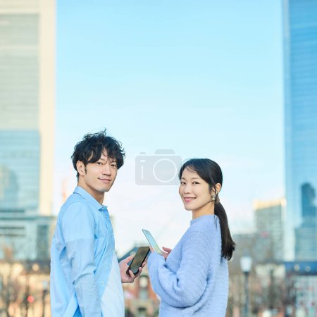 Téléchargez les photos : Homme et femme souriants avec smartphone à la main le beau jour - en image libre de droit